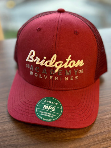 Dark red trucker hat with "Bridgton" in white embroidered cursive text, with ACADEMY on the second line and WOLVERINES on the third line.